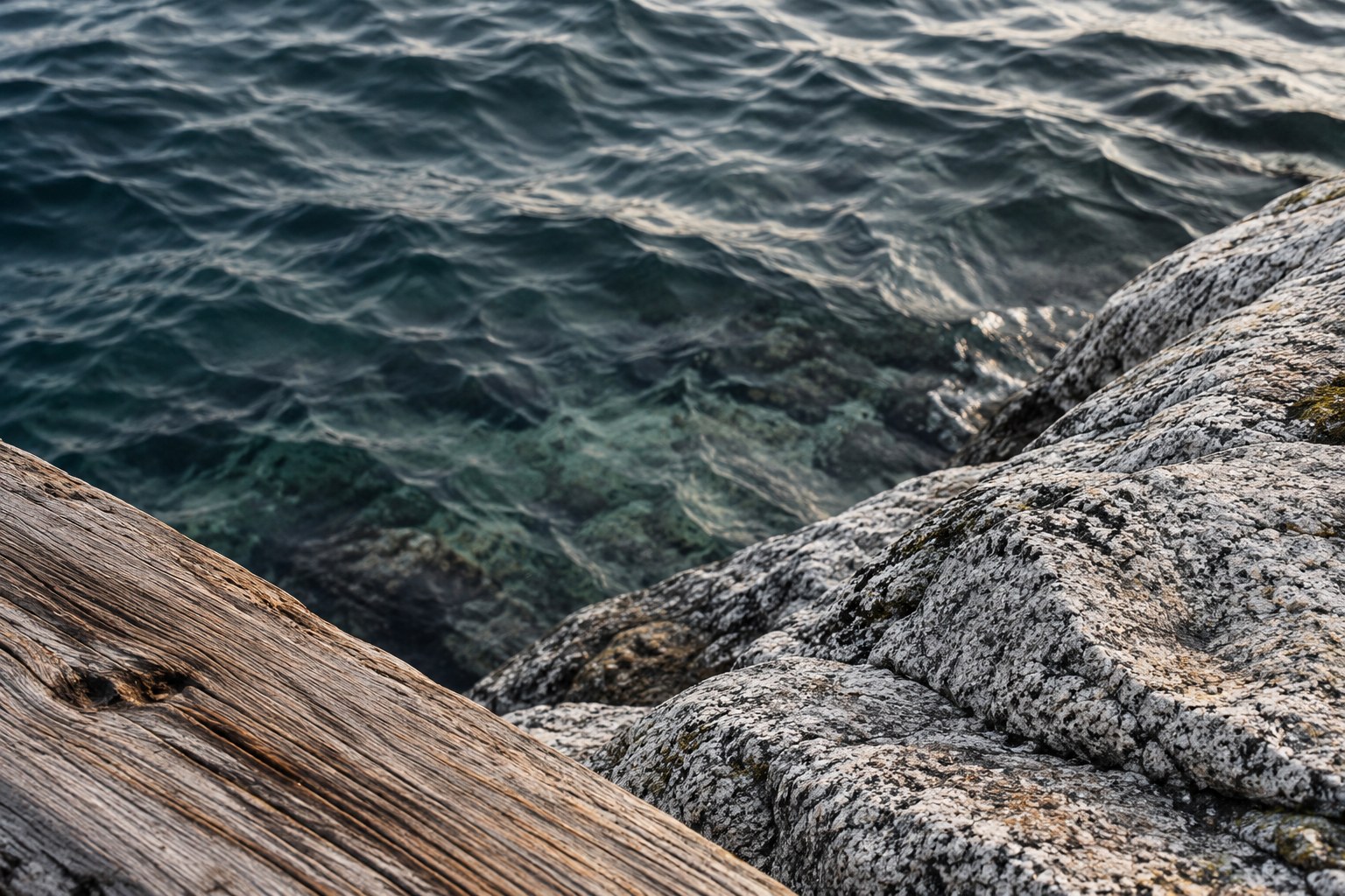 An abstract coastal study of weathered wood, granite, and rippling water